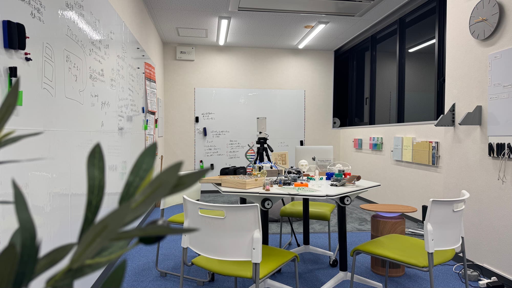 手書きでびっしり埋まったホワイトボードの壁に囲まれたオリジナルスクールの教室。中央のテーブルにDNA模型や分子模型、周期表などの実験材料が並ぶ